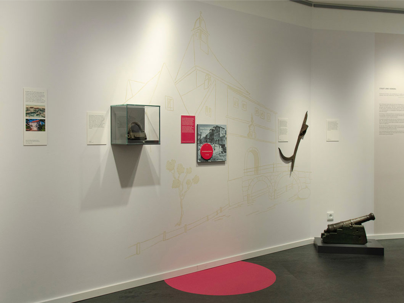 Rote Markierungen an Ausstellungsstationen weisen auf Spuren der Geschichte um das Bildnispaar.